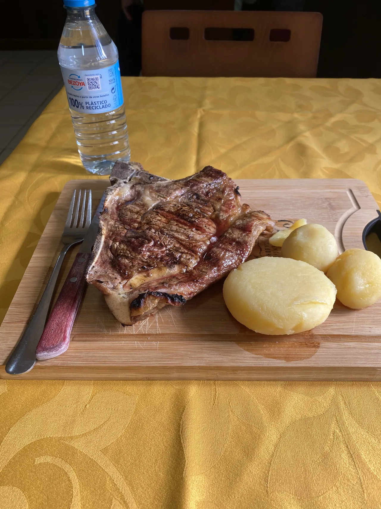 Pieza de carne con hueso y patatas servida sobre una tabla en El Bosque