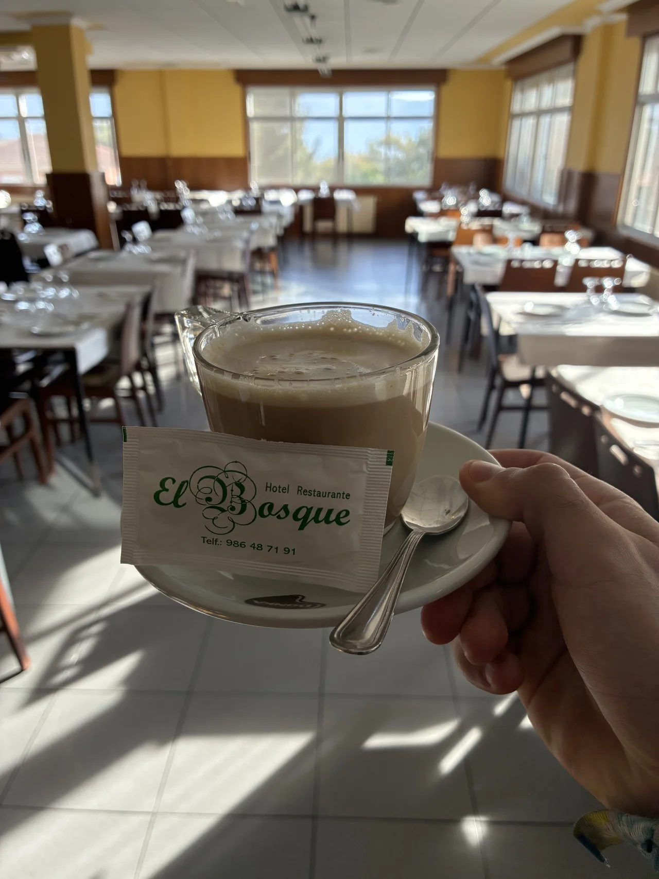 Taza de El Bosque sostenida delante de las mesas del comedor